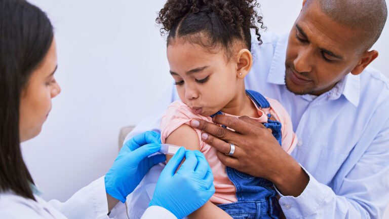Child with her parent getting bandage placed on her arm by a pharmacist.