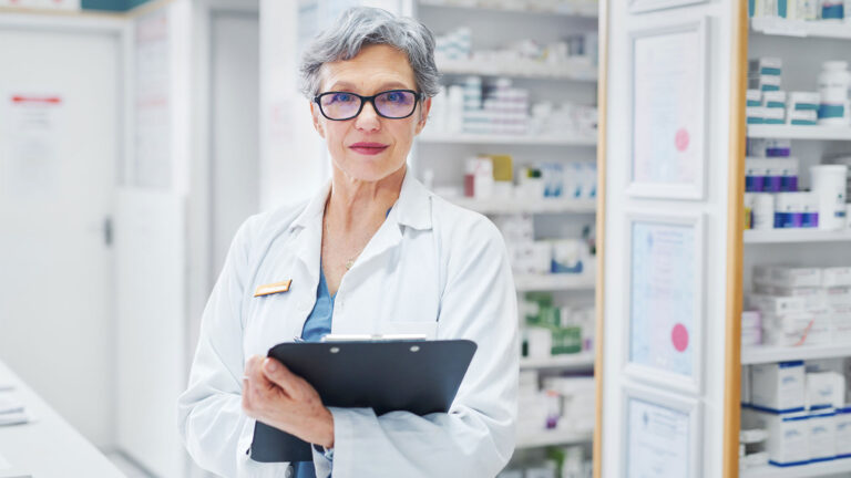 Pharmacy licensee standing in the pharmacy with clipboard.