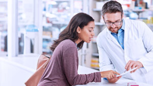 Pharmacy professional helping patient reviewing prescription in the pharmacy.